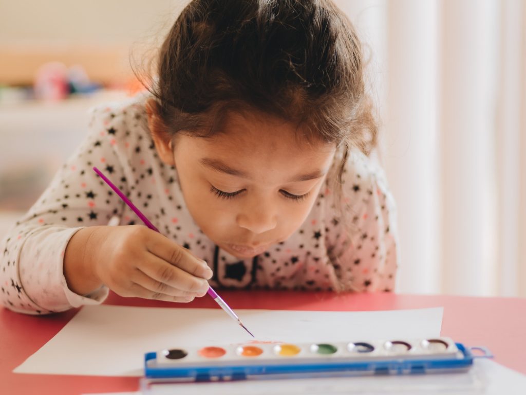 Pretty diverse pre school girl at home painting with water colors